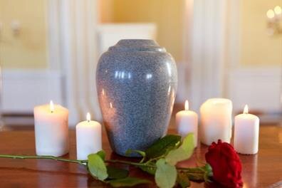 Candles surround a vase on a table while a single rose rests beside it in a quiet setting.