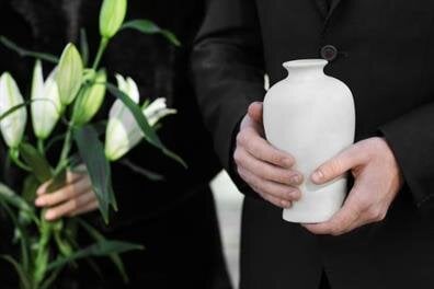 People stand together holding flowers and an urn as they pay their respects at a memorial service.