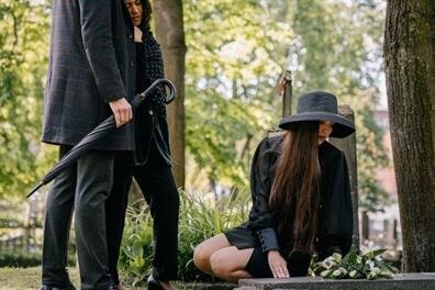 A woman kneeling on a grave with a man holding an umbrella