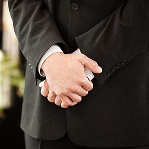 A person in a dark suit stands with hands clasped, creating a formal atmosphere at the event.