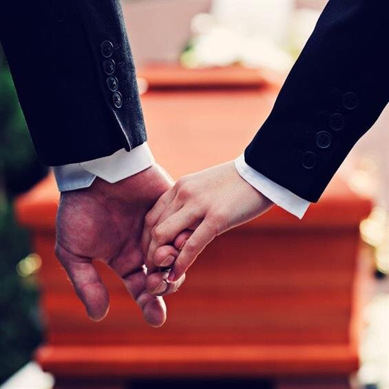 A couple holds hands by a casket during a memorial service.