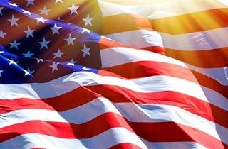 The American flag billows in the wind, shining brightly as sunlight streams through the fabric.