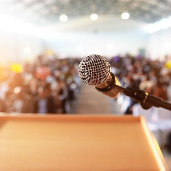 A microphone awaits on a podium as the eager audience anticipates the speaker.