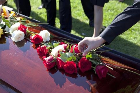 Groups of people gather to pay respects at a burial site, placing roses on a casket.