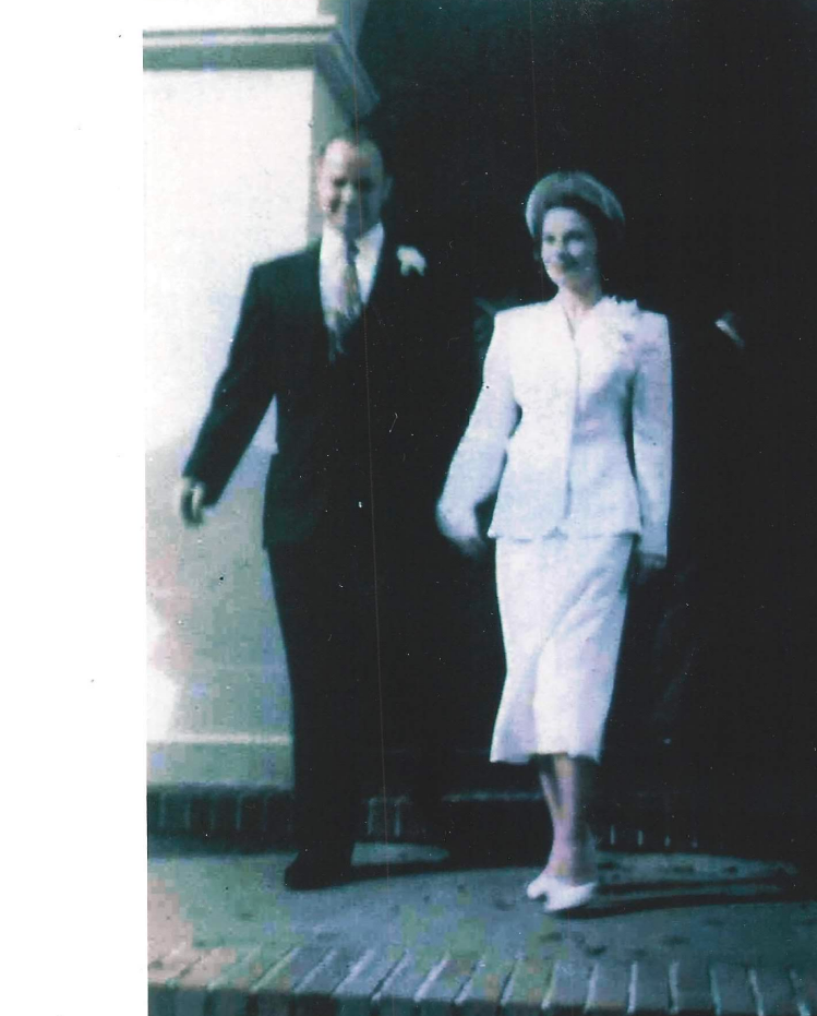 A couple joyfully walks out of a building, dressed elegantly for their wedding day celebration.