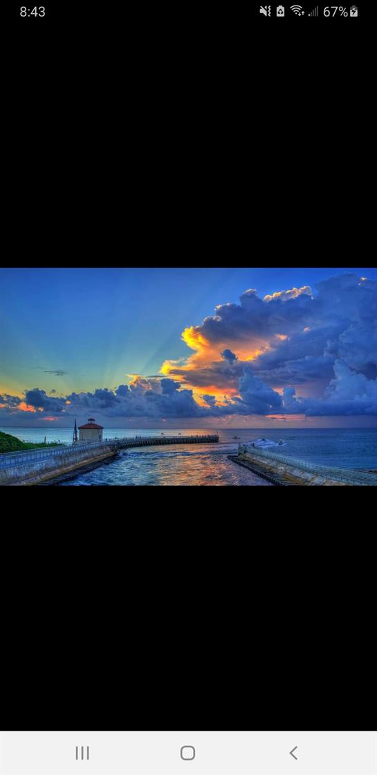 Waves gently lap against the pier as a vibrant sunset colors the sky above the ocean.