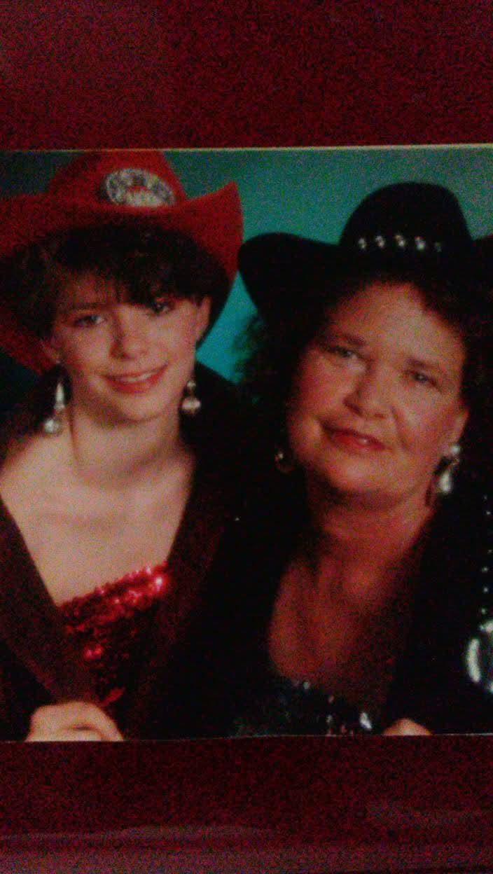 Two smiling women wear stylish cowboy hats and colorful outfits while celebrating together.