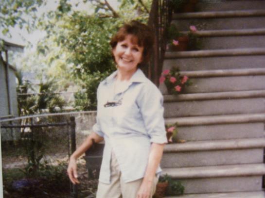 Woman cheerfully stands by garden steps, enjoying a sunny afternoon amid greenery.