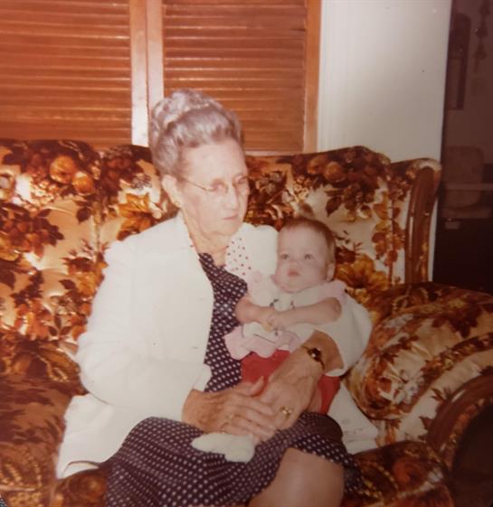 An older woman cradles a baby on a patterned sofa rich with memories.