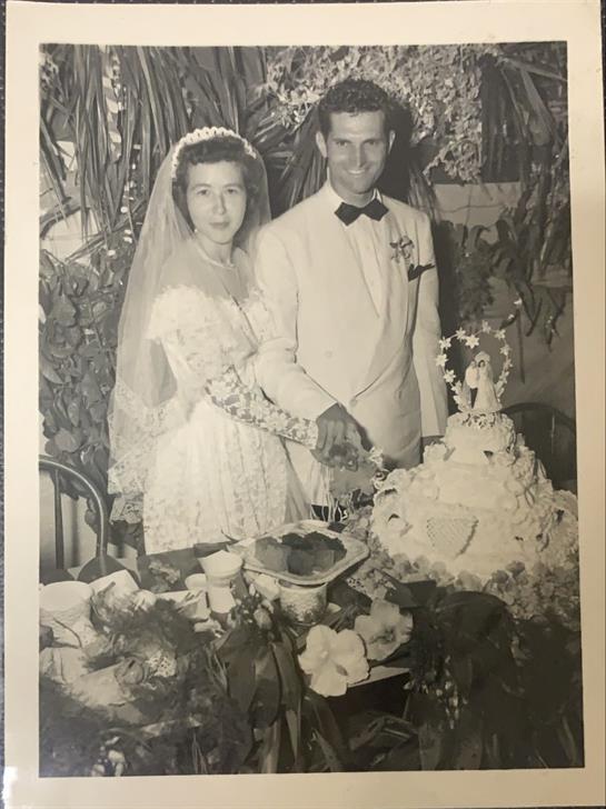 Newlyweds joyfully cut their wedding cake surrounded by greenery and festive decor.