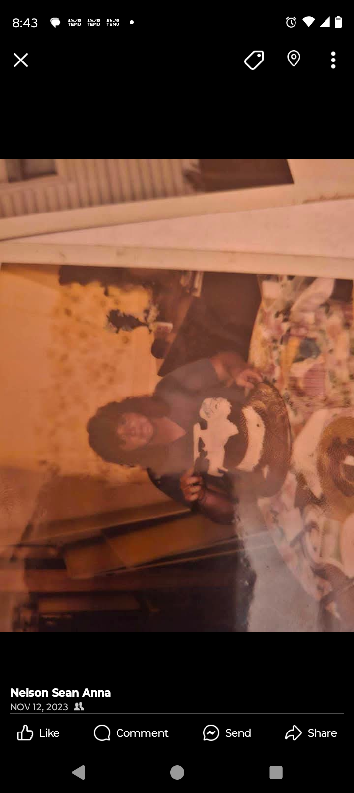 A woman smiles while holding a cake surrounded by friends in a warm, inviting space.