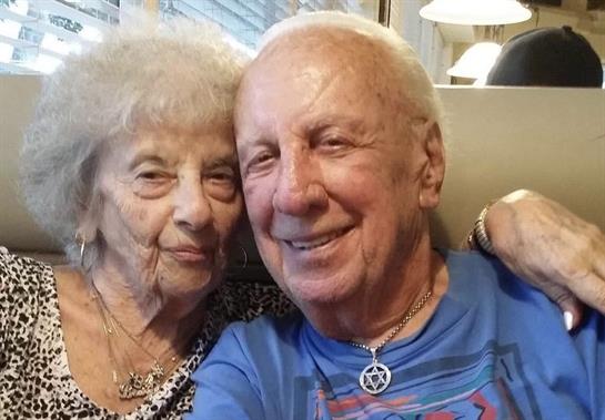 Two seniors smile warmly at each other, celebrating a joyful moment in a casual dining setting.