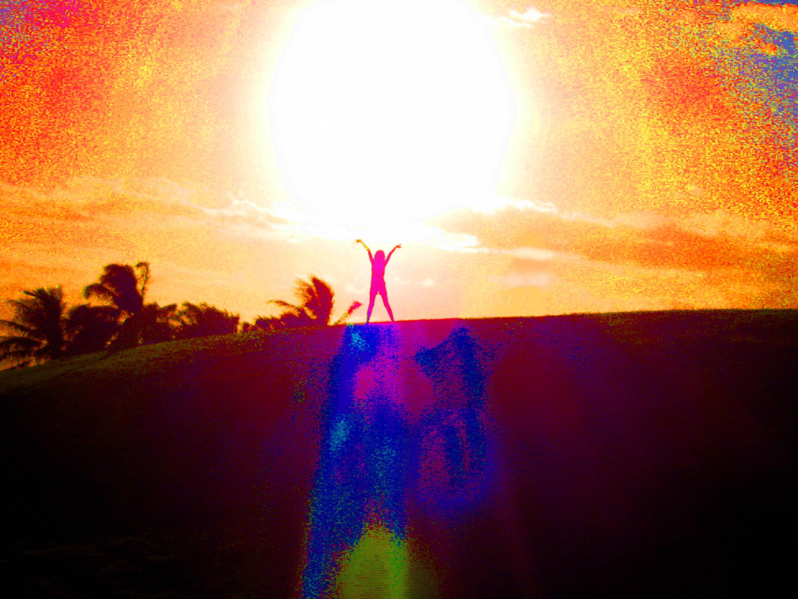 A person stands on a hilltop with arms raised joyfully against a vibrant sunset backdrop.