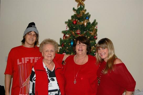 Four family members stand together smiling by a Christmas tree decorated with ornaments.
