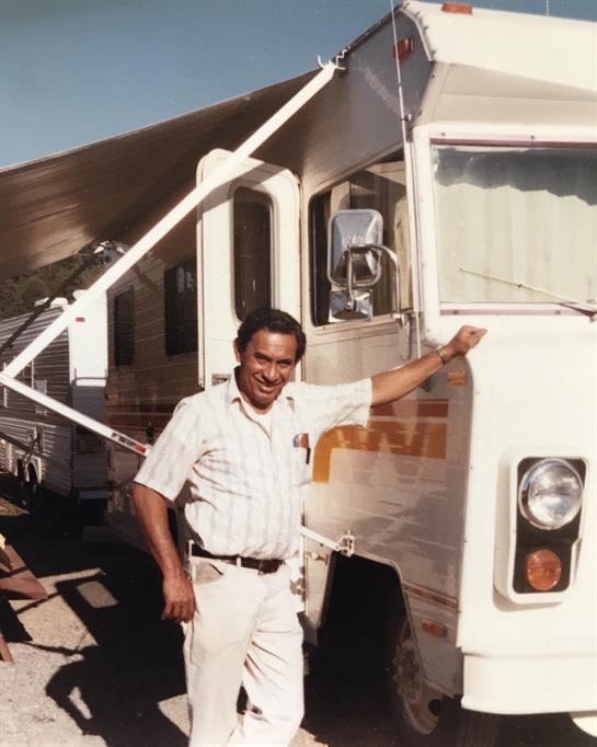 A man poses next to a camper truck parked during daytime in a rural area.