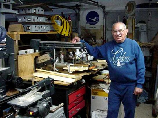 Man works on woodworking tasks in a garage filled with various tools and equipment.