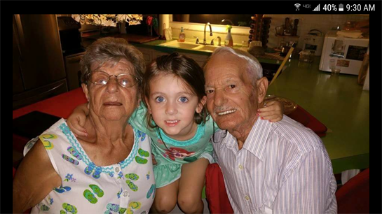 Grandparents smile as their grandchild sits between them in a cozy kitchen.