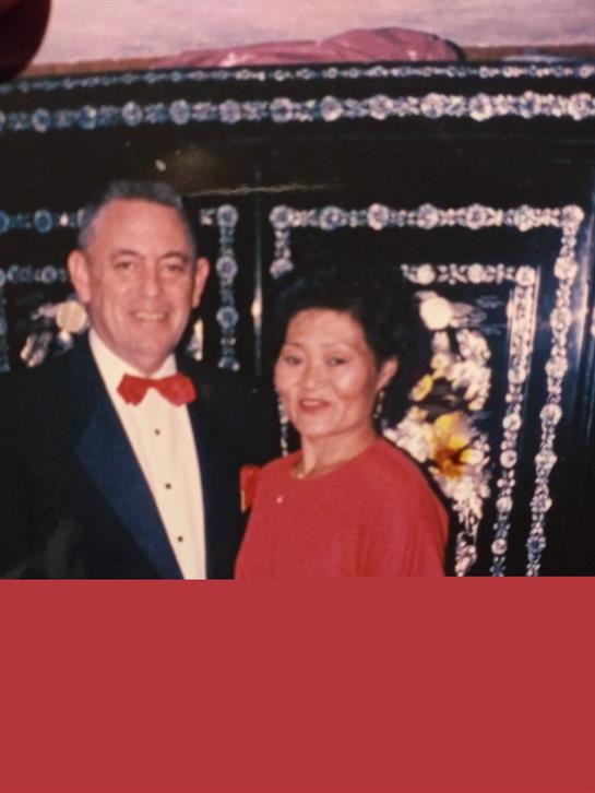 Couple dressed in formal wear poses joyfully at a vibrant event with colorful decor.