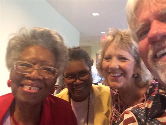 Four friends share laughter and smiles during a cheerful reunion in a well-lit space.