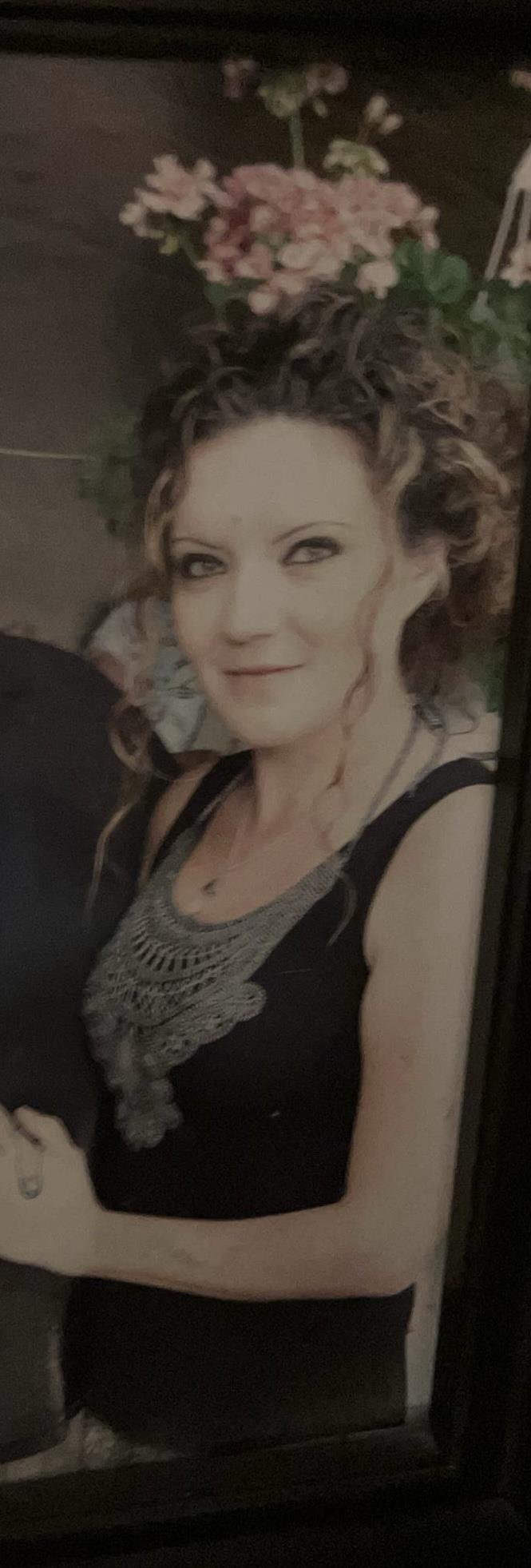 A woman with curly hair smiles warmly while showcasing her intricate jewelry at a gathering.