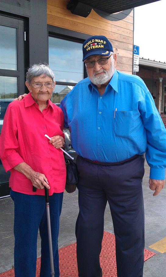 Elderly man and woman stand smiling outside a building, enjoying each other's company.