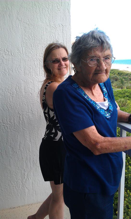 Two women enjoy time together on a balcony, while the sea is visible in the background.