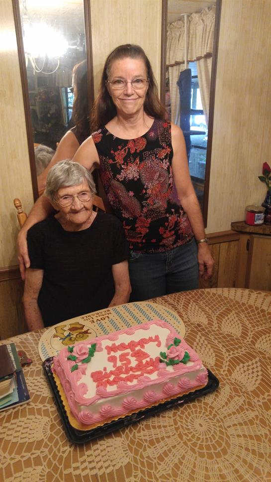 Two women share a moment at a table with a cake celebrating a special occasion during the daytime.