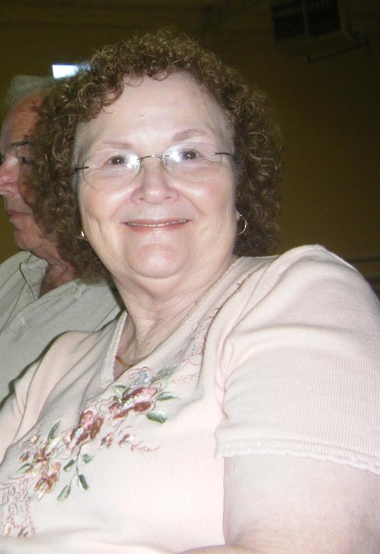 Woman with curly hair smiles warmly while seated next to a man in a social setting.