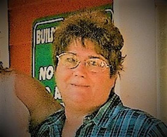 A woman wearing a plaid shirt and glasses smiles confidently against a vibrant wall backdrop.