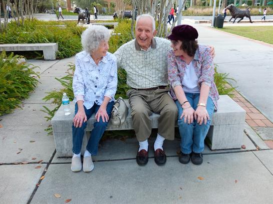 Three seniors sit on a bench in a park, engaging in joyful conversation and companionship.