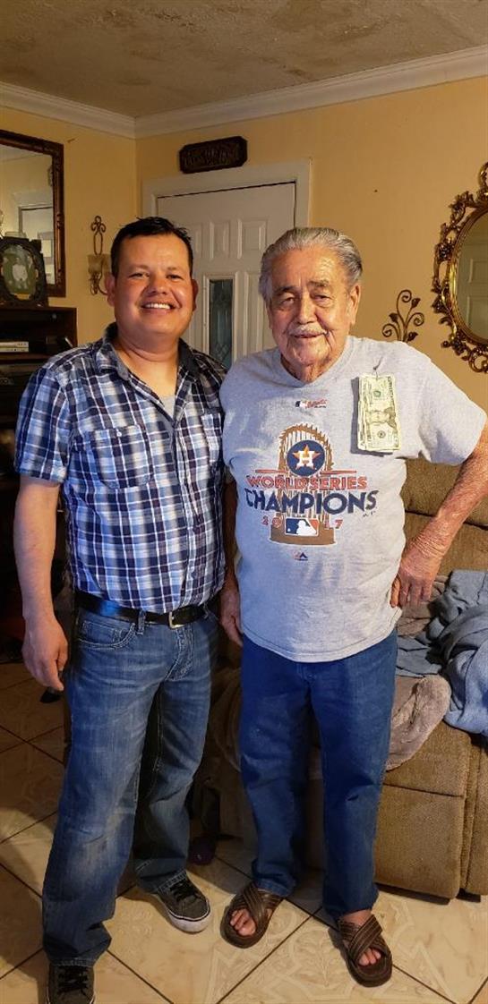 Two men stand side by side in a cozy living room, smiling happily and enjoying each other's company.