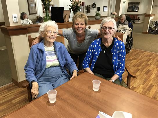 Three joyful seniors share laughter and companionship at a care home in the afternoon.