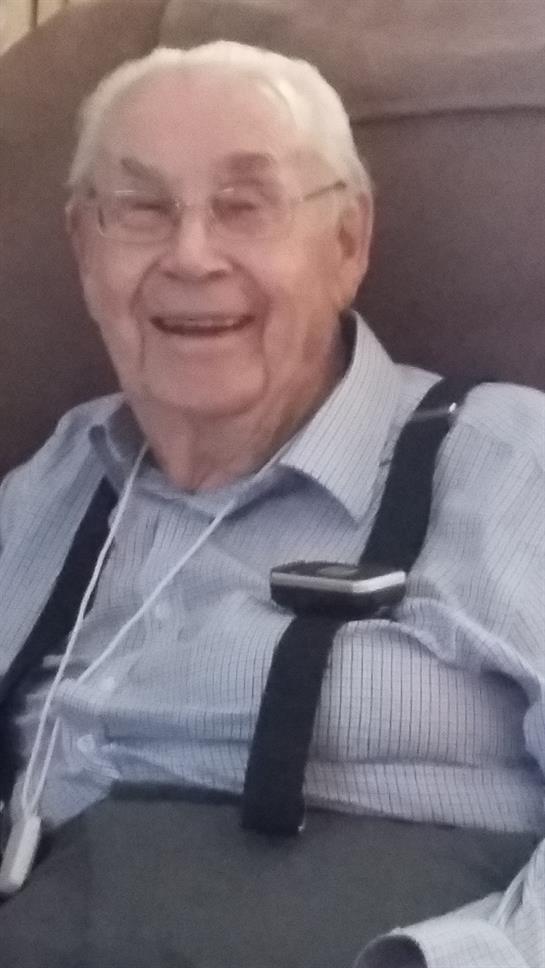 Elderly man smiles warmly in casual attire while sitting comfortably in a relaxed environment.