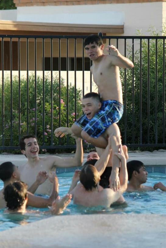 Children are playing in a pool, lifting each other in games while laughing and having fun.