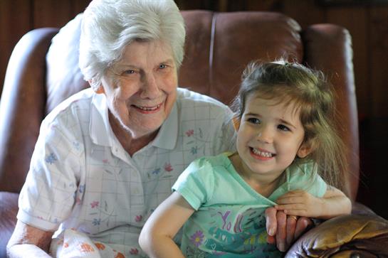 A smiling grandmother and her cheerful granddaughter share a moment of joy on a couch.