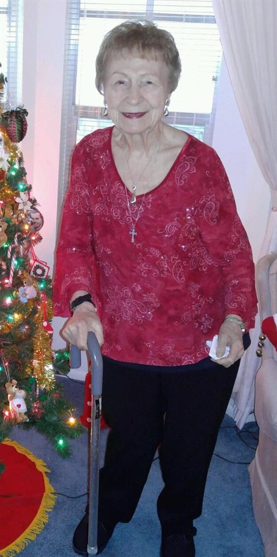 An elderly woman with a walker stands by a festive Christmas tree, embracing holiday cheer.