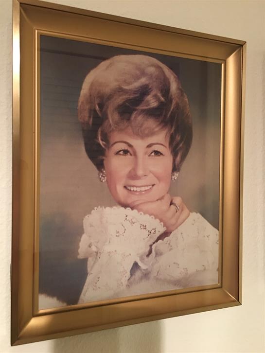 A cheerful woman poses with a soft smile, showcasing a stylish hairstyle and classic attire.