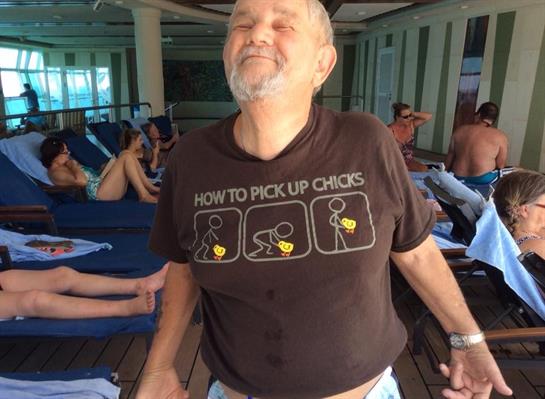 The man smiles proudly while showcasing his playful t-shirt at a lively pool location.