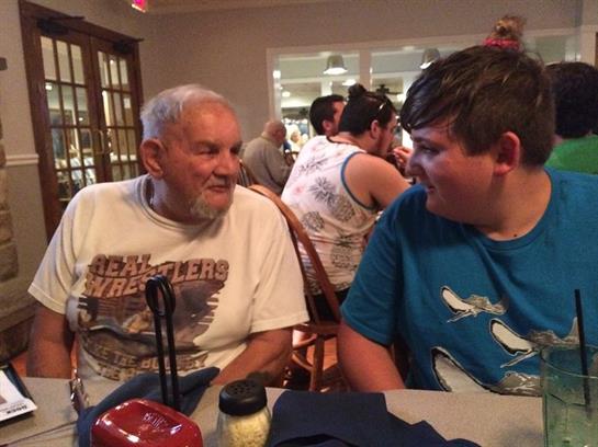 An elderly man chats happily with a young boy in a busy restaurant.