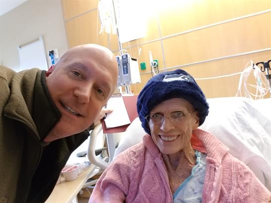 A joyful caregiver takes a selfie with a patient in a hospital room, brightening their day.
