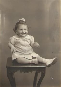 A young child with curly hair poses happily on a wooden stool, showcasing a vintage style.