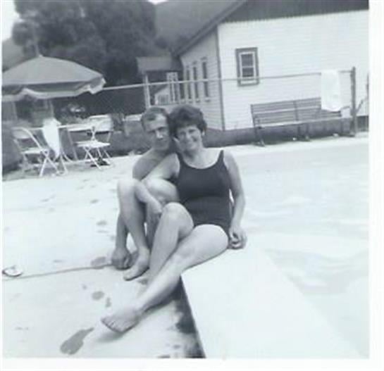 A couple is seated at the pool's edge, soaking up the sun and enjoying their carefree summer day.