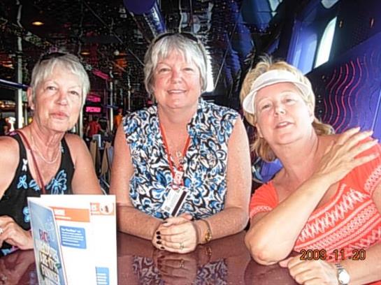 Three cheerful women gather at a table, smiling and sharing stories in a vibrant restaurant.