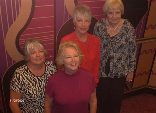 Four women are joyfully posing for a picture at a vibrant social event in a festive setting.
