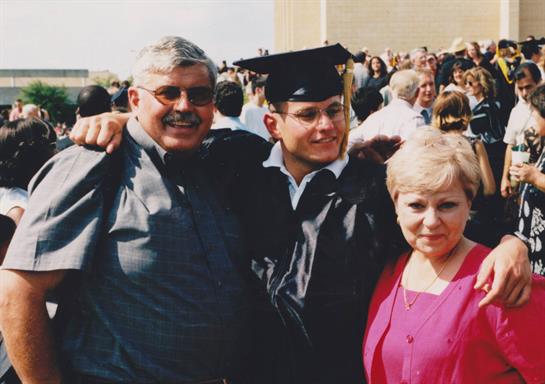 A proud graduate celebrates their achievement outdoors with family.