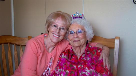 Two women share a heartfelt moment, smiling and celebrating a birthday in a cozy indoor setting.