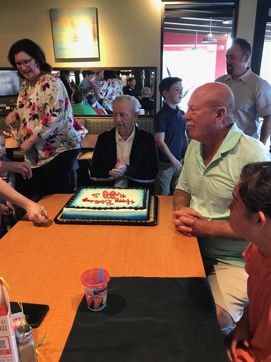Family gathers around to celebrate a birthday with cake and laughter in a lively restaurant setting.