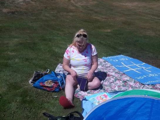 A woman is enjoying a sunny afternoon sitting on a picnic blanket in a park.