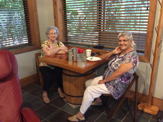 Two women sit at a wooden table, smiling and chatting while enjoying their coffee and snacks.
