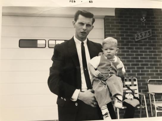 A father stands proudly with his young son outside their home, showcasing familial love.